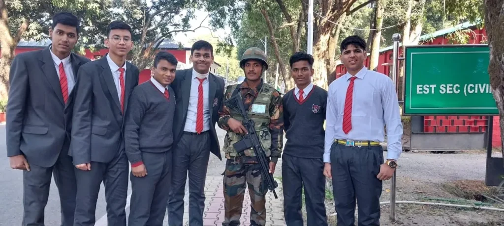 Six students in school blazers, sweaters and red ties stand beside a soldier in camouflage uniform and helmet who is carrying a rifle