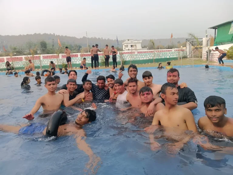 Students on an outing, in an outdoor swimming pool with a tyre tube floating nearby and hills in the background